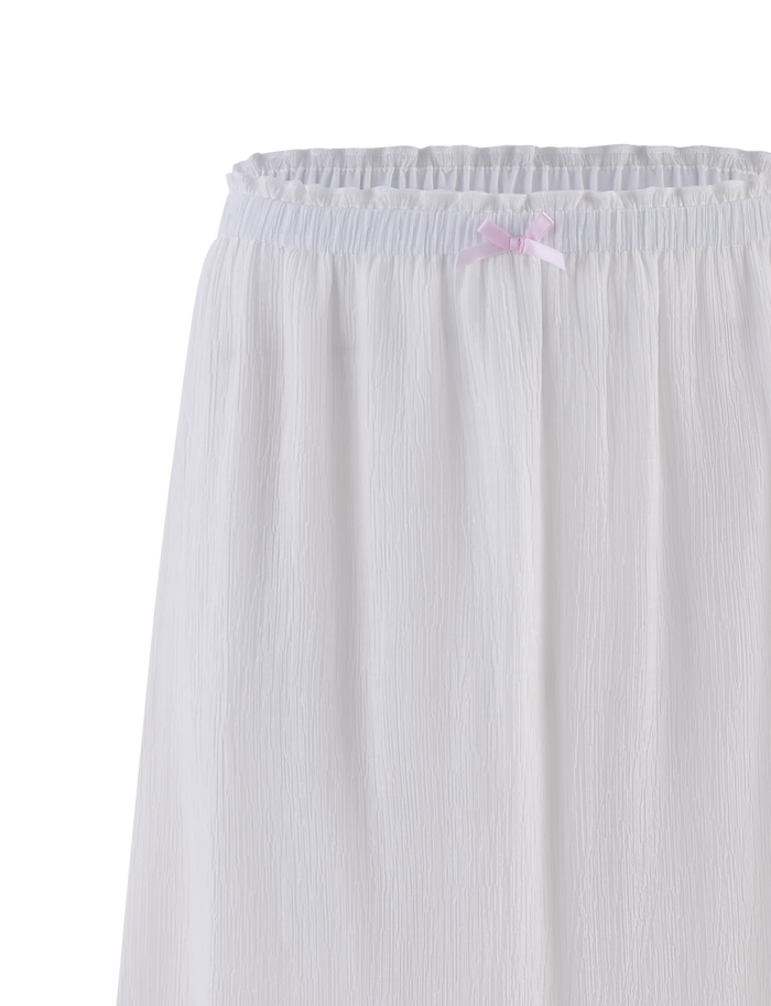 The ASHLYNN MAXI SKIRT by TIGERMIST features a white crinkled design, an elasticated waist, and a contrast satin bow at the top center. Its lightweight, semi-sheer fabric gives it a delicate, airy look.