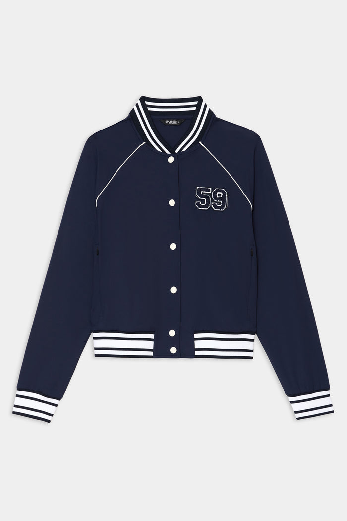The SPLITS59 Hayes Varsity Rigor Jacket in indigo is crafted from a comfy nylon-spandex blend, featuring white striped cuffs, collar, and hem, a "59" chest patch, and white snap buttons down the front.
