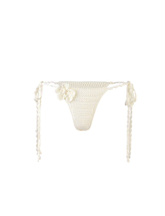 The MELIORA BIKINI BOTTOM - WHITE from TIGERMIST features adjustable side ties and small crocheted flower details on one side. This high-cut thong style bikini bottom showcases intricate crochet patterns, embodying a delicate, handmade aesthetic that is characteristic of TIGERMIST’s signature designs.