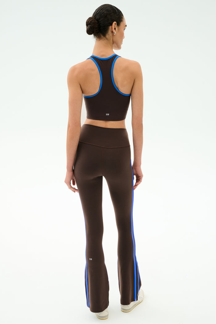 A woman faces away, wearing SPLITS59's Raquel High Waist Supplex Flare leggings in Dark Chocolate/Classic Blue—perfect for gym sessions—against a plain white background.
