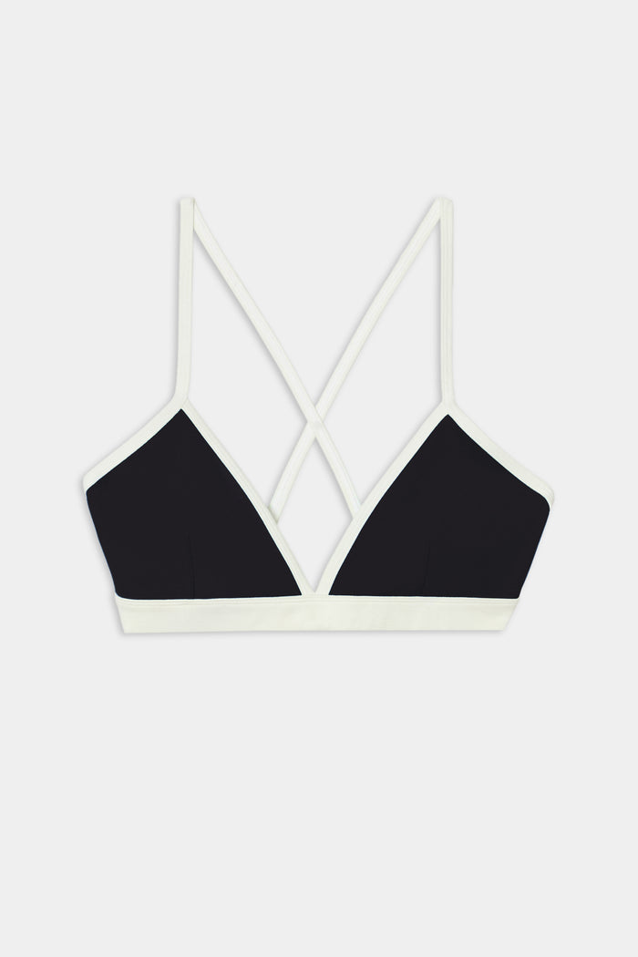 The SPLITS59 Sage Rigor Bra in Black/White is crafted from a soft nylon-spandex blend, featuring thin double straps that cross at the back and white trim, displayed on a white background.