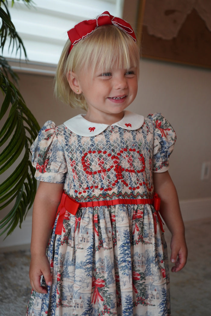Girl wearing The Polar Express Bow Girl Handsmocked Dress with red hair bow