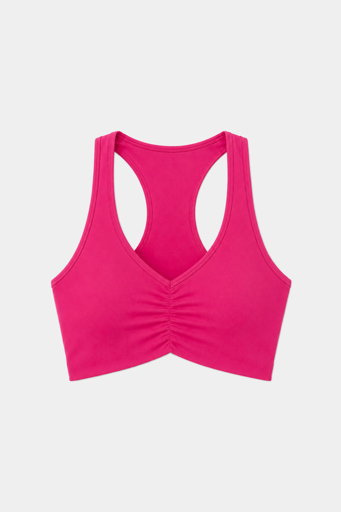 The SPLITS59 Airweight Bra with Ruching in Sangria is a vibrant pink racerback sports bra crafted from stretchy nylon-spandex activewear, featuring a ruched front detail and shown on a plain white background.