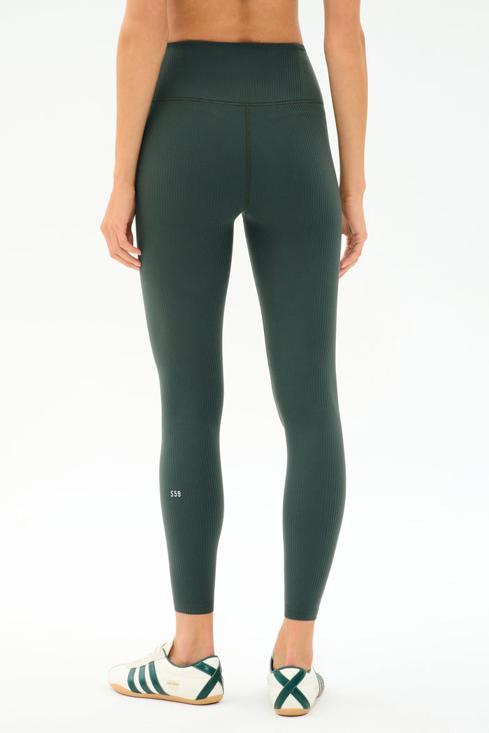 Person faces away, wearing SPLITS59 Airweight Rib High Waist 7/8 leggings in Military and white sneakers with green detail, against a plain light background.