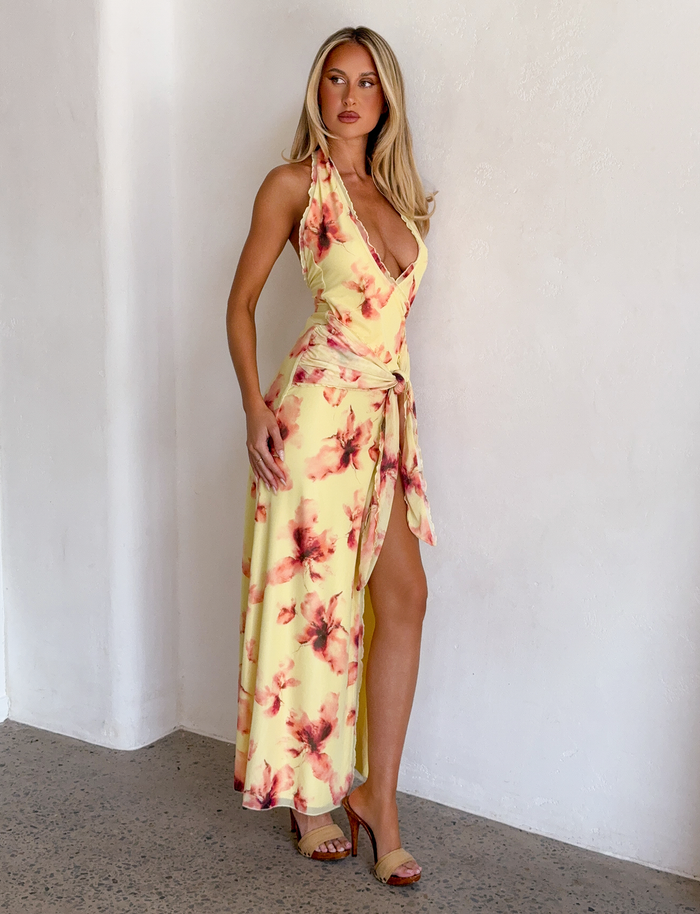 A woman in the TIGERMIST ALLEGRA MAXI DRESS in yellow watercolour floral print, featuring a plunging halter neckline.