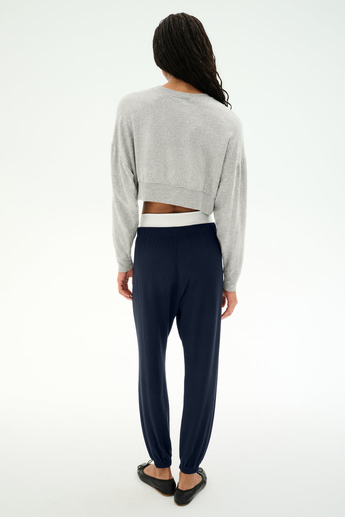 A person stands against a white background, facing away; wearing a gray cropped sweatshirt, SPLITS59 Andie Dual Waist Sweatpant in Indigo/White—made in Los Angeles—and black flats.