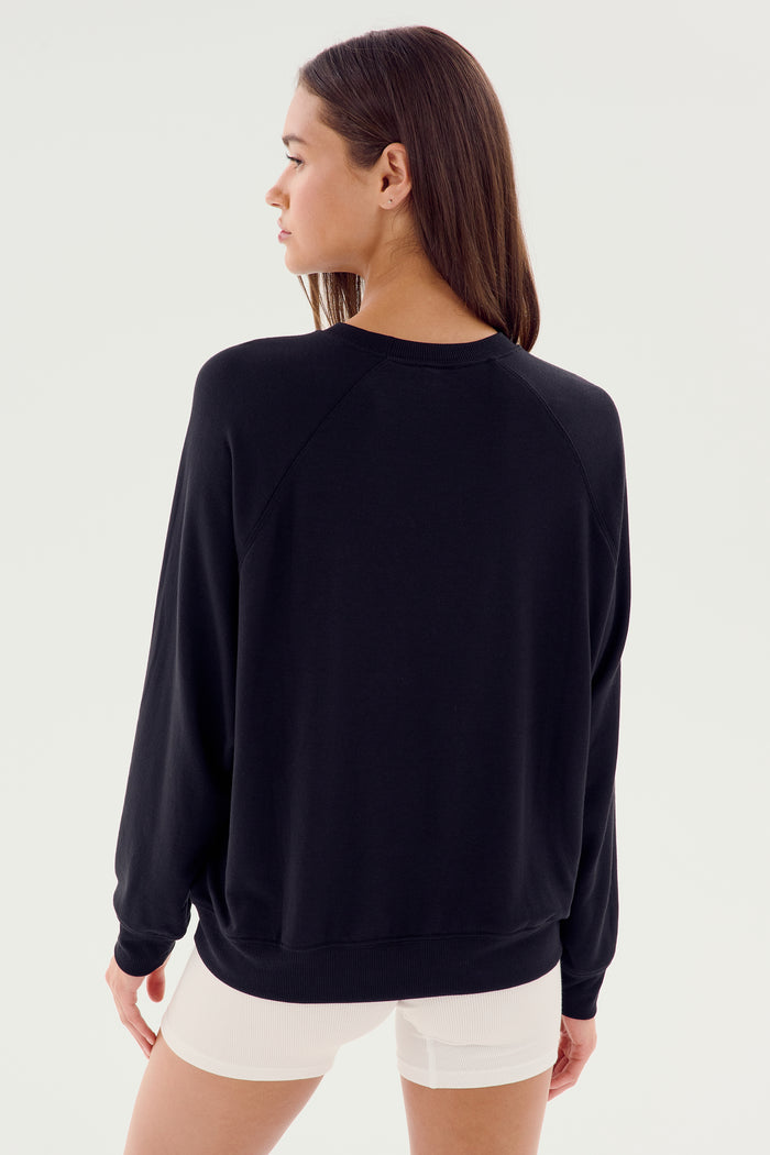 A person with long brown hair wearing an SPLITS59 Andie Fleece Sweatshirt - Black and white shorts made in Los Angeles, facing away from the camera.