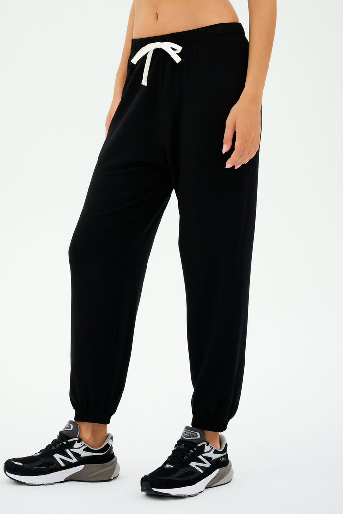 Dressed in SPLITS59's Andie Oversized Fleece Sweatpant - Black with a white drawstring and black sneakers, perfect for cool-weather workouts. Made in Los Angeles, these joggers offer both style and comfort with every step.