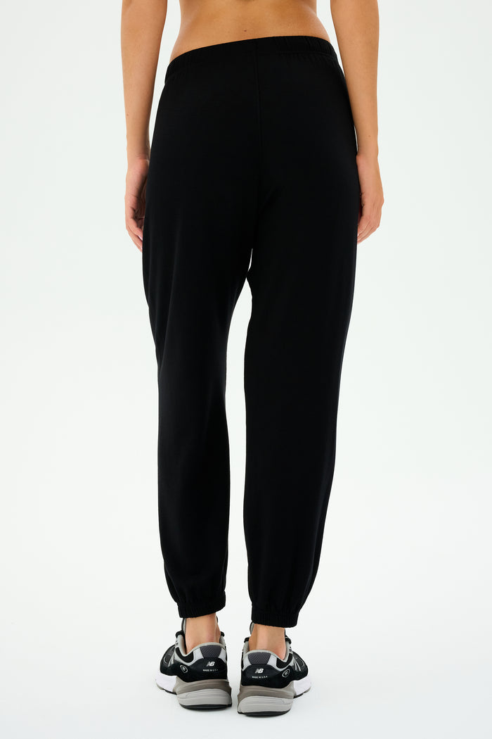 Back view of a person wearing SPLITS59's Andie Oversized Fleece Sweatpant in Black and black sneakers, ideal for cool weather workouts.