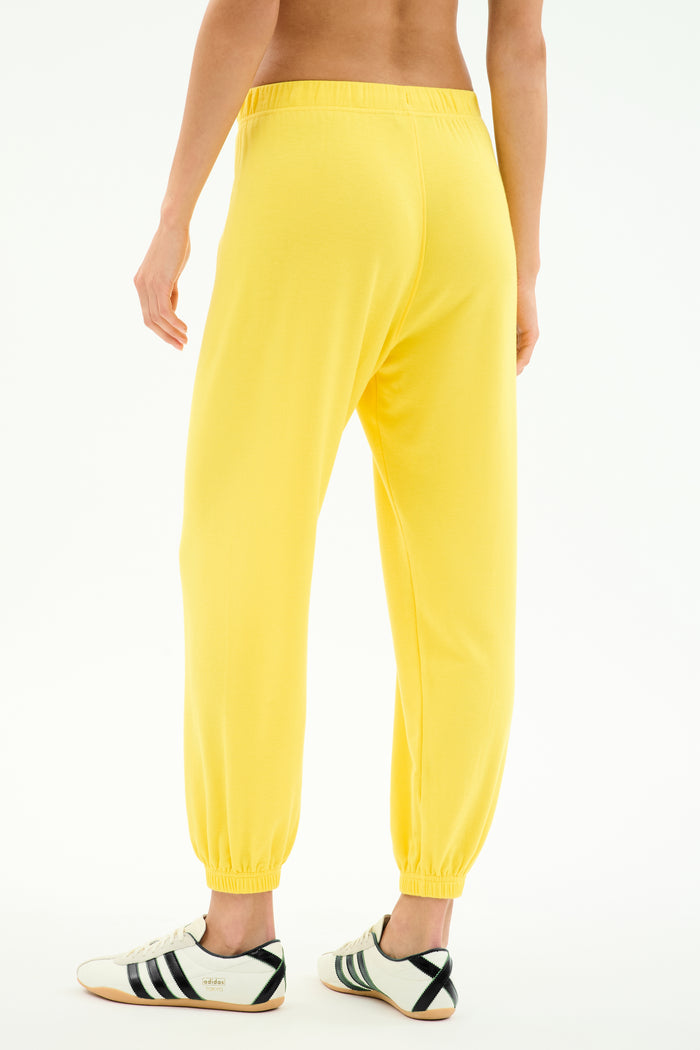 Model wears SPLITS59 Andie Oversized Fleece Sweatpant in bright yellow, paired with white sneakers with black stripes, shown from the back against a plain white background.