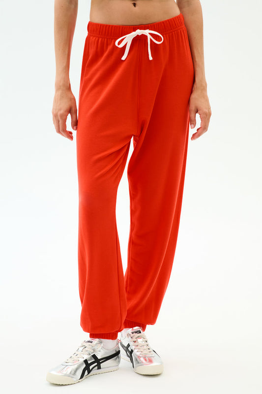 Person wearing SPLITS59 Andie Oversized Fleece Sweatpant in Lotus Red with a white drawstring and silver sneakers, perfect for warm weather workouts, standing against a white background.