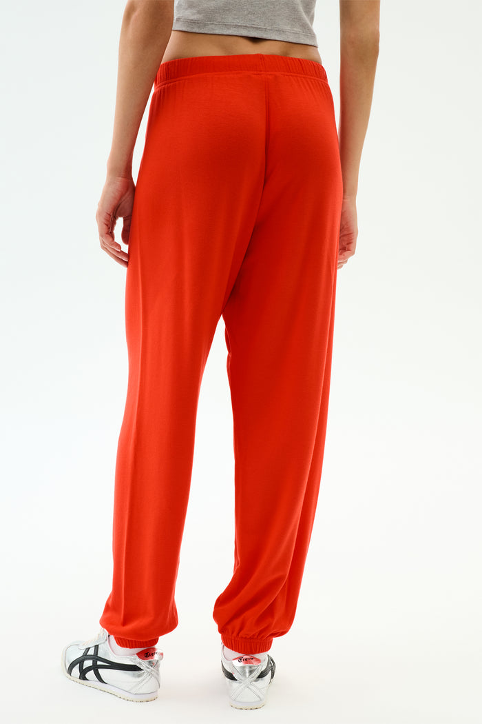 A person wears the SPLITS59 Andie Oversized Fleece Sweatpant in Lotus Red with a gray crop top and white athletic shoes, standing against a plain light background—a vibrant, comfortable choice for warm weather workouts.