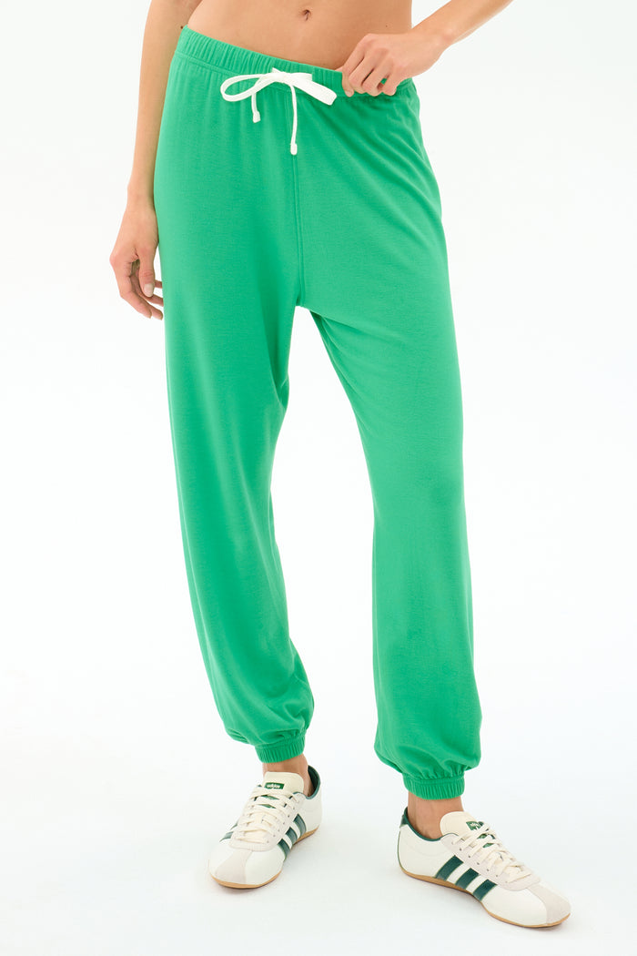A person wears the SPLITS59 Andie Oversized Fleece Sweatpant in Spearmint, featuring a white drawstring, paired with white sneakers with green stripes—ideal for cool weather workouts—standing against a plain white background.