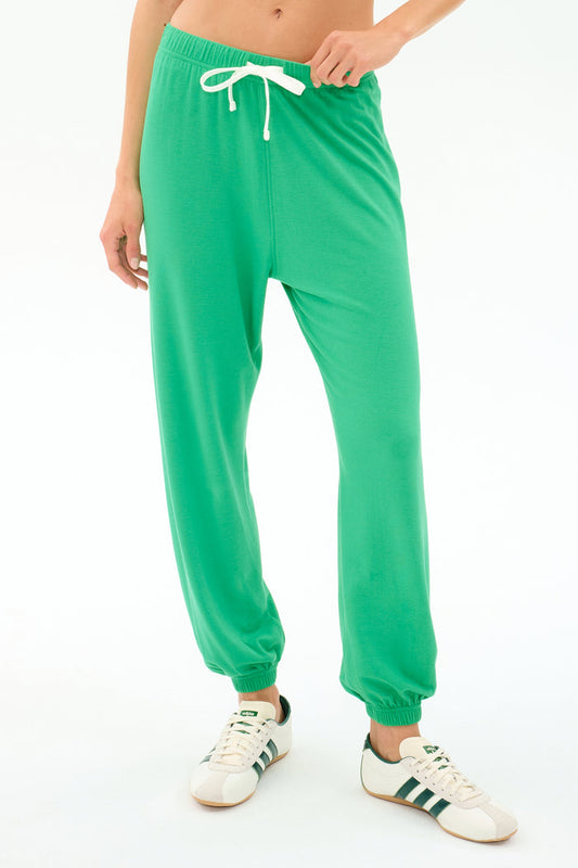 A person wears the SPLITS59 Andie Oversized Fleece Sweatpant in Spearmint, featuring a white drawstring, paired with white sneakers with green stripes—ideal for cool weather workouts—standing against a plain white background.