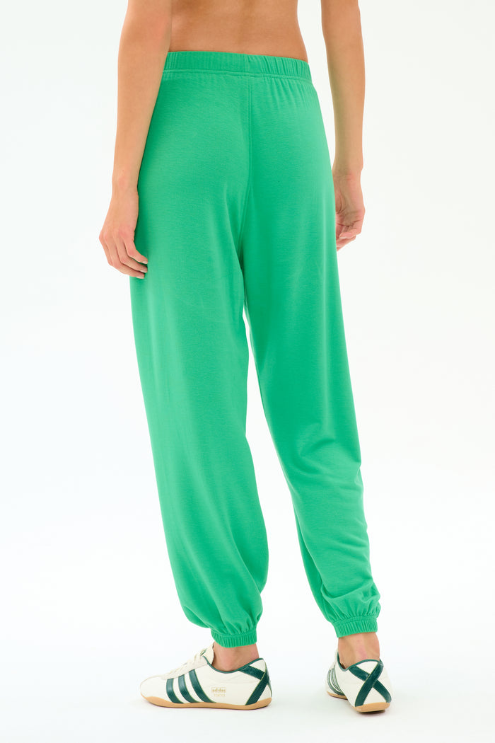 Model wears the SPLITS59 Andie Oversized Fleece Sweatpant in Spearmint, shown from the back with white sneakers accented by green stripes, against a plain white background.