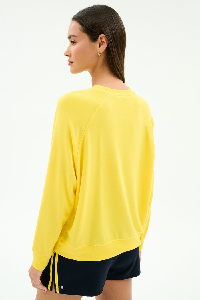 A woman faces away, wearing the SPLITS59 Andie Oversized Fleece Sweatshirt in bright yellow and dark spandex blend shorts with yellow side stripes, against a plain light background.