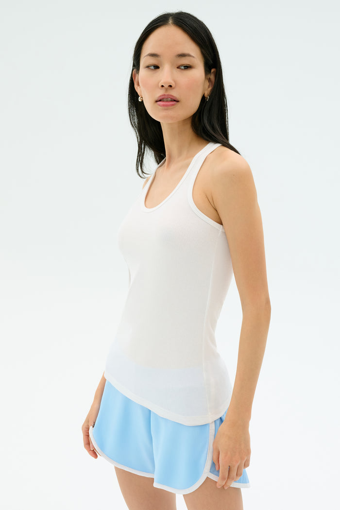 A woman stands against a plain background wearing the Splits59 Ashby Rib Tank in white and light blue athletic shorts, looking slightly to the side.