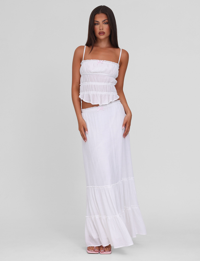 Woman with long dark hair wearing TIGERMIST's ASHLYNN MAXI SKIRT in white, a tiered maxi skirt with an elasticated waist, styled with a white ruffled sleeveless crop top, standing against a plain light background.