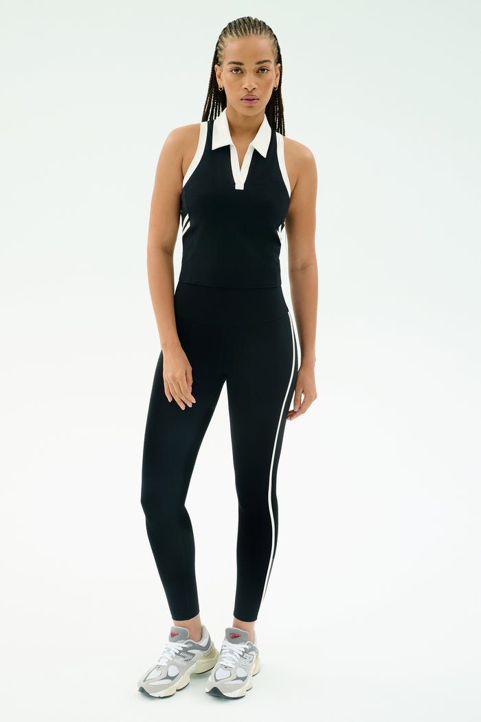 A person stands against a plain background wearing the SPLITS59 Amber Airweight High Waist 7/8 leggings in Black/White.