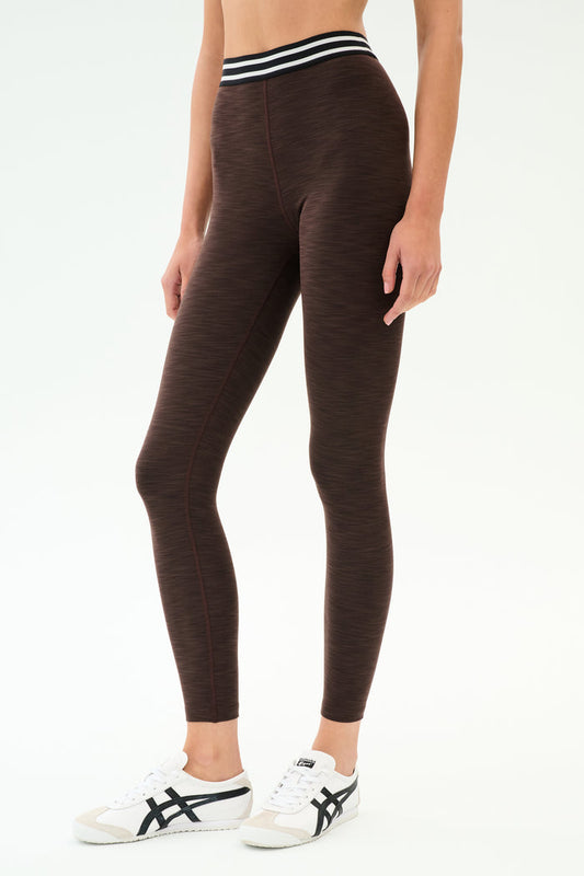 A person wears SPLITS59's Bailey High Waist Active Rib 7/8 leggings in Heather Dark Chocolate with a black-and-white striped waistband and white sneakers against a plain white background—ideal for gym sessions.