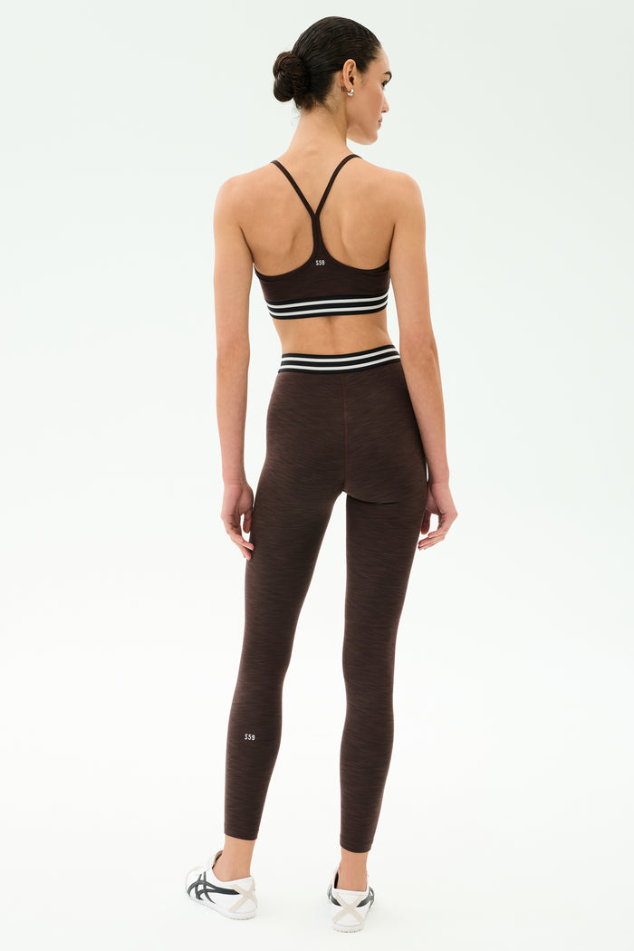 A person wears the SPLITS59 Bailey High Waist Active Rib 7/8 leggings in Heather Dark Chocolate, facing away against a plain light background—ideal activewear for gym workouts.