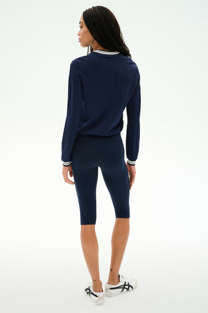A person stands facing away, wearing the SPLITS59 Bonnie Knit Half Zip in Indigo/White, paired with matching navy knee-length leggings and white sneakers with black accents, against a plain white background.