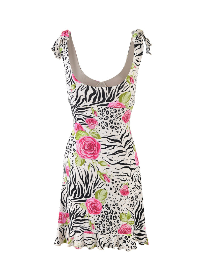 The BRYNNE DRESS - MULTI : ZEBRA from TIGERMIST is a sleeveless, knee-length dress featuring an eclectic mix of zebra, cheetah, and rose patterns. It boasts a deep scoop neckline, tied shoulder straps, and alternating black and white animal prints adorned with vibrant pink roses. The hemline is slightly flared for added style.