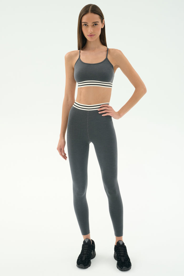 A woman wears the SPLITS59 Cali Active Rib Bra in Heather Grey with matching leggings and black sneakers against a plain white background.
