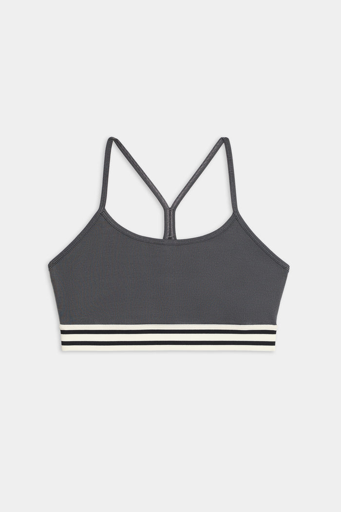 The Cali Active Rib Bra by SPLITS59 features a gray ribbed design, thin shoulder straps, a racerback, and a white-and-black striped elastic band at the bottom.