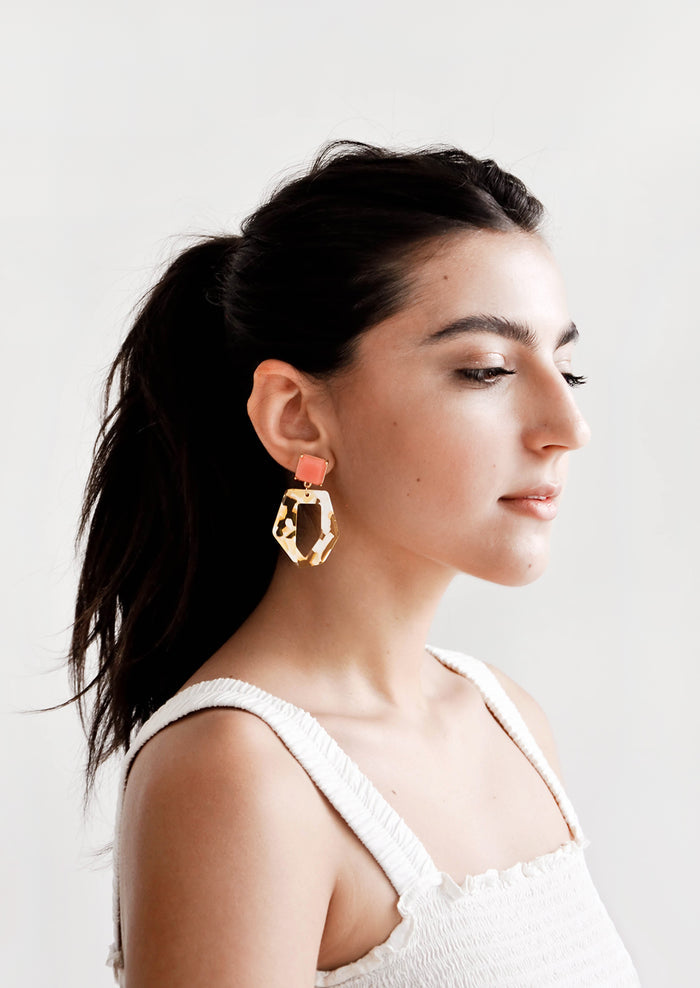 Model wears yellow, white, and coral pink drop earrings and white tank top.
