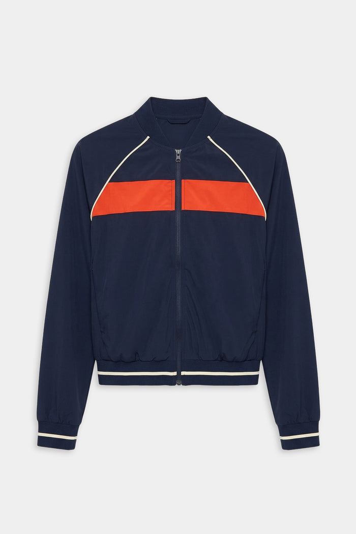 The SPLITS59 Carrie Woven Nylon Jacket in Indigo/Lotus Red features a zip-up design with a bright red chest stripe and white piping on the shoulders and cuffs, crafted from spandex and nylon.