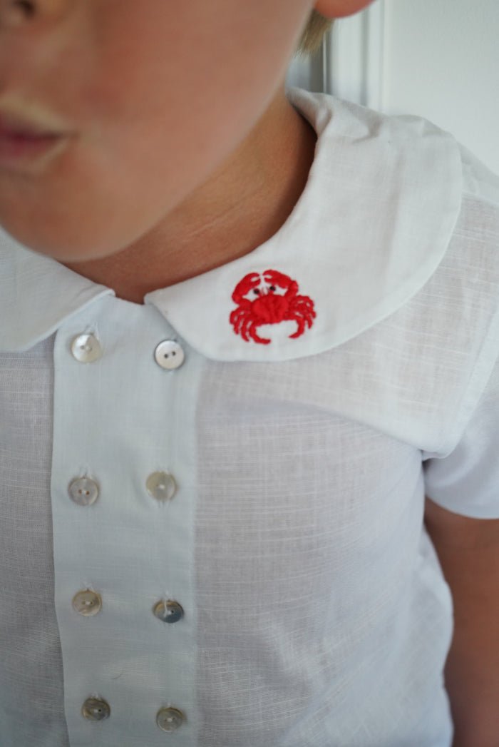 Close-up of embroidered crab detail on white linen shirt