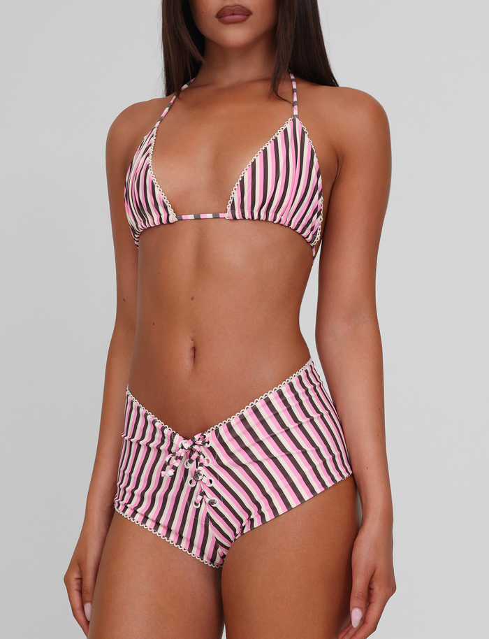 A woman models the TIGERMIST DAZZLE BIKINI TOP - STRIPE, featuring pink, black, and white stripes with scallop lace trim and lace-up high-waisted bottoms, against a plain light gray background.