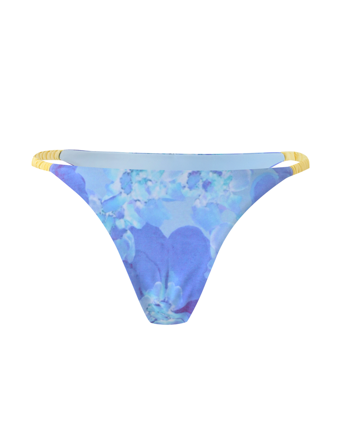 The TIGERMIST EMBERLAIN BIKINI BOTTOM - BLUE MACRO FLORAL features a low-rise bodycon fit with blue floral print and thin yellow side straps, shown on a white background.
