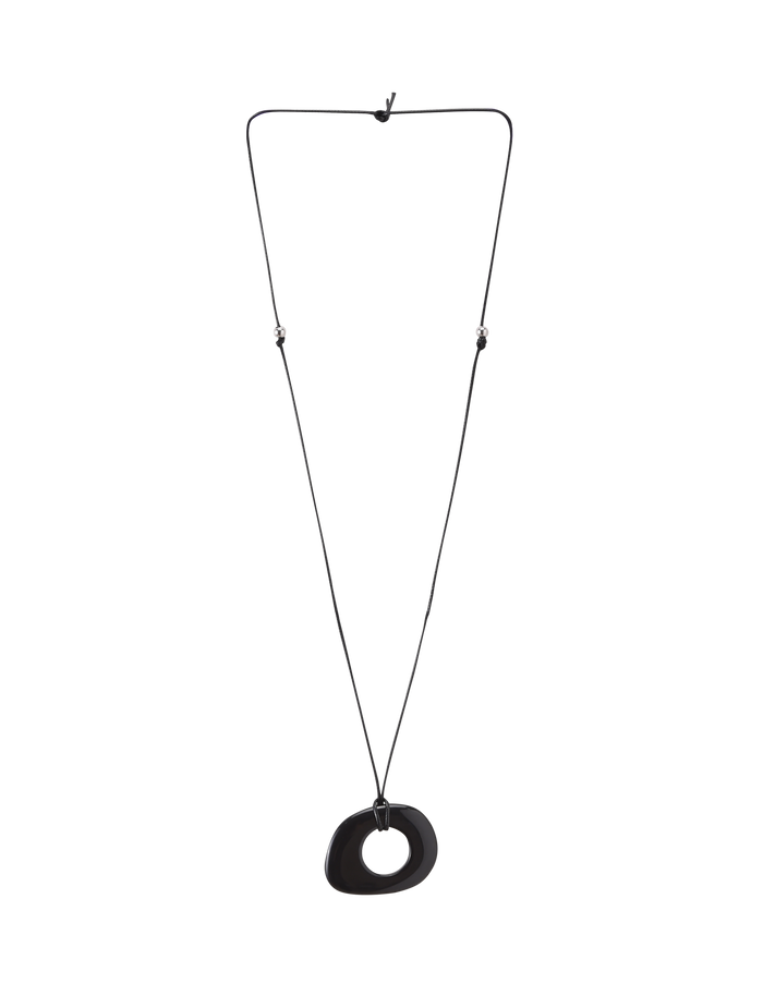 The FAELLA PENDANT NECKLACE - BLACK by TIGERMIST features a minimalist, irregular black resin pendant with a central hole on an adjustable cord, shown against a plain white background.
