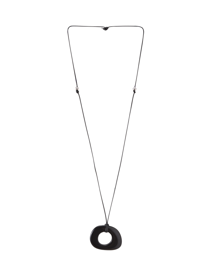The FAELLA PENDANT NECKLACE - BLACK by TIGERMIST features a long, thin adjustable cord with two small beads and a large smooth black resin pendant with an off-center hole, shown against a plain white background.