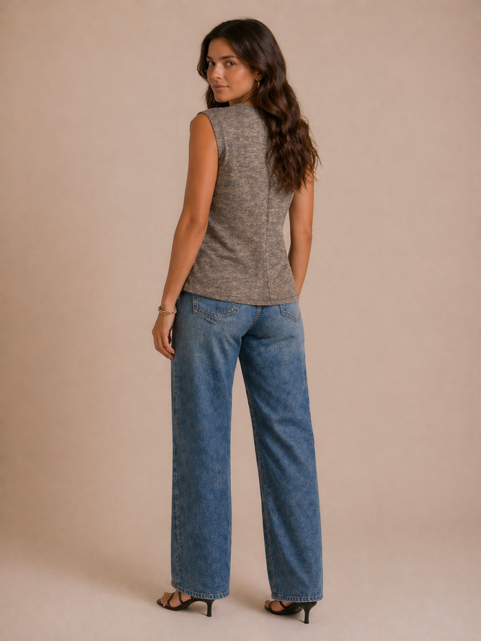 Woman wearing a sleeveless gray top and blue jeans against a beige background