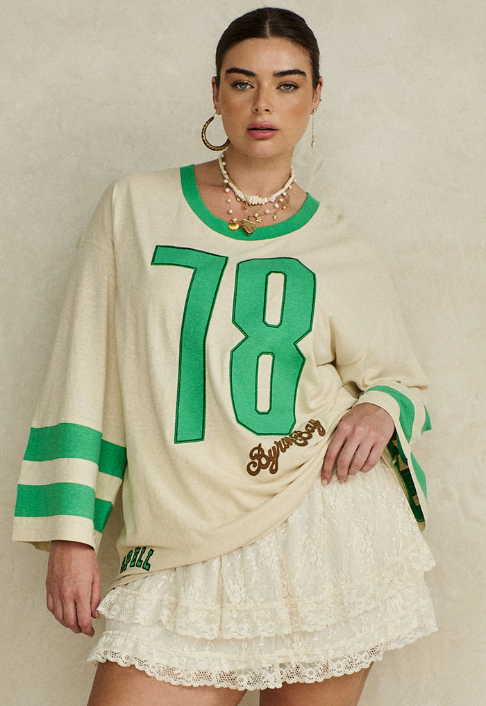 Model wearing Homecoming Long Sleeve Biker Tee, front view showing number 78 applique and green sleeve stripes