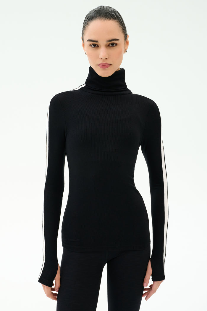 A woman faces forward against a white background, wearing the SPLITS59 Jackson Rib Full Length Turtleneck in Black/White with matching black pants.