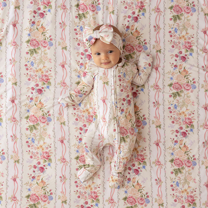 Baby lying on a Janey print fabric backdrop, wearing a matching floral convertible one-piece with a bow headband