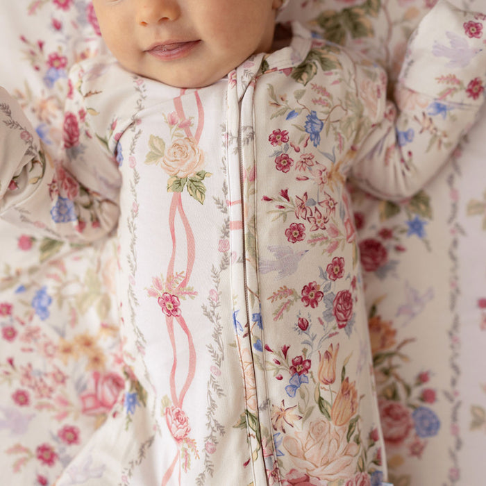 Close-up of a baby lying down wearing the Janey print convertible one-piece, showing the floral pattern and ruffle detail