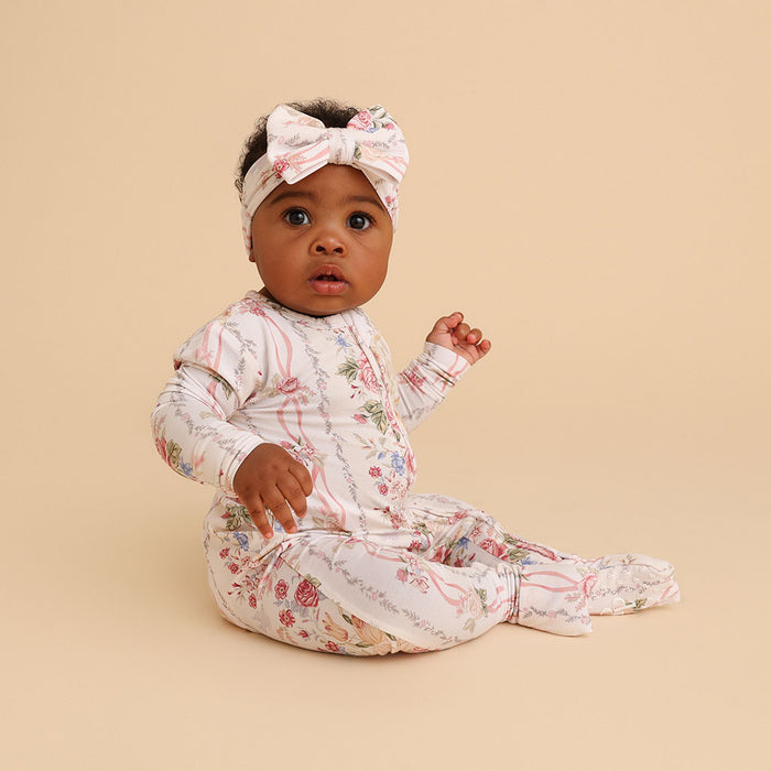 Baby sitting up wearing the Janey print convertible one-piece with fold-over mittens, on a cream background