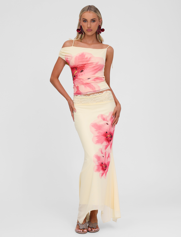 A woman with long blonde hair models the TIGERMIST LILLIAN SKIRT in yellow, paired with a cream off-shoulder top and posing with one hand on her hip against a plain white background.