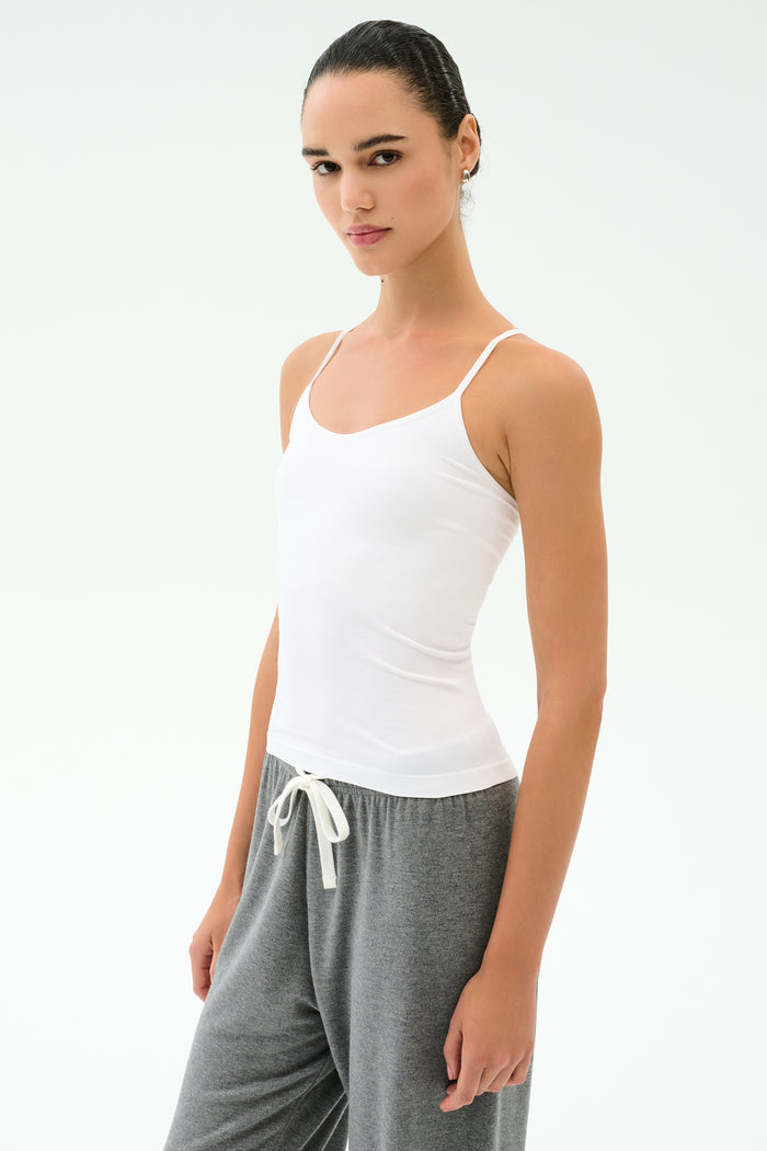 A person stands slightly sideways against a plain background wearing the SPLITS59 Loren Seamless Waist Length Tank in white and gray drawstring pants.