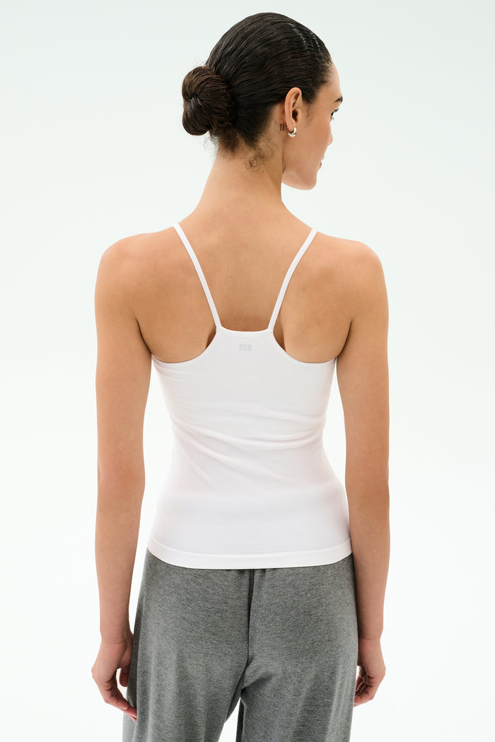 A person faces away, wearing the SPLITS59 Loren Seamless Waist Length Tank in white and gray pants, hair tied back in a low bun, set against a plain light background.