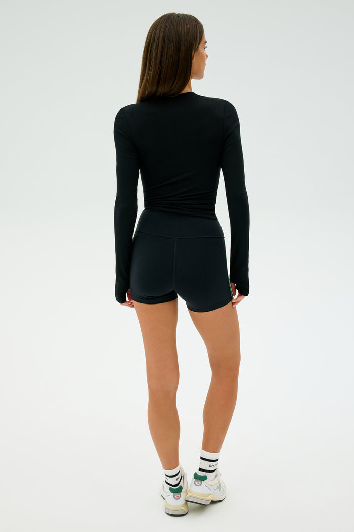 A person in the Louise Rib Long Sleeve - Black from SPLITS59, part of the MADE IN LOS ANGELES collection, and white sneakers stands facing away on a plain background.