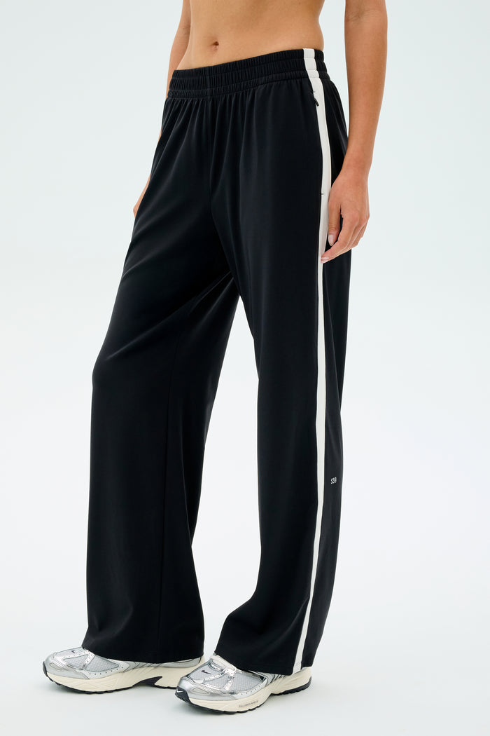A person wearing the SPLITS59 Maxie Rigor Track Pant in Black/White with silver sneakers stands against a plain background.