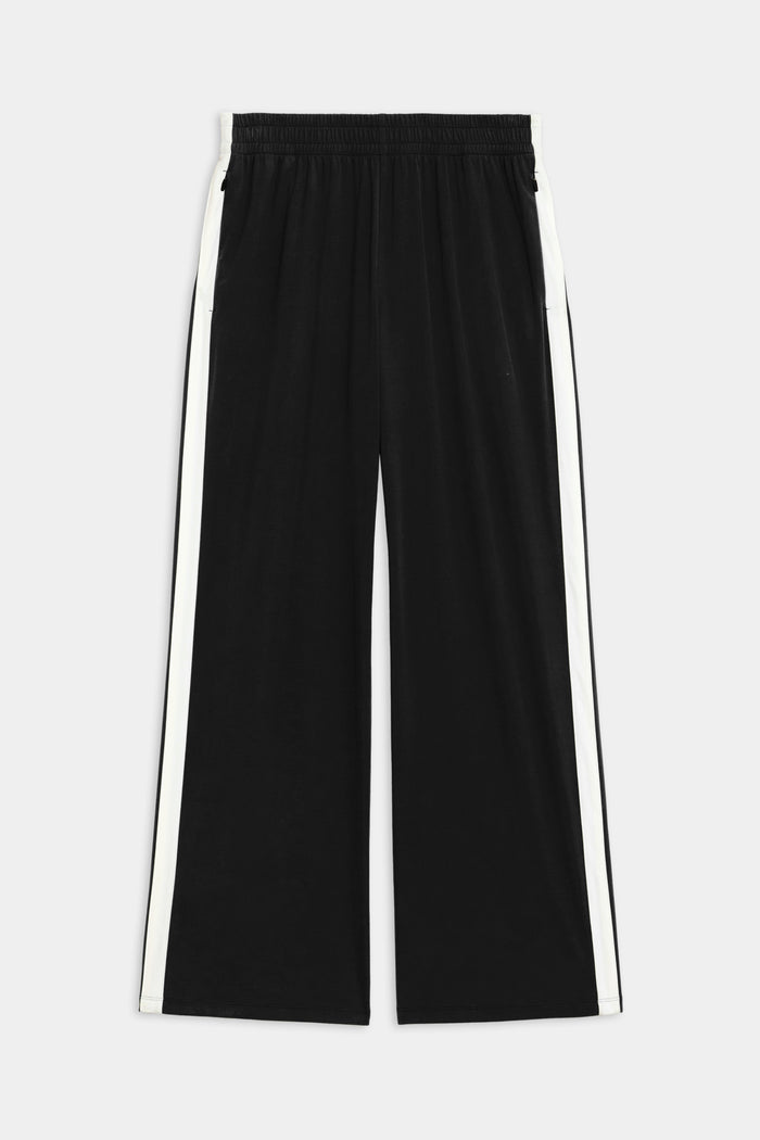 The SPLITS59 Maxie Rigor Track Pant - Black/White showcases a wide-leg silhouette, white side stripes, elastic waistband, and two side pockets, made from durable Rigor fabric and displayed on a plain background.