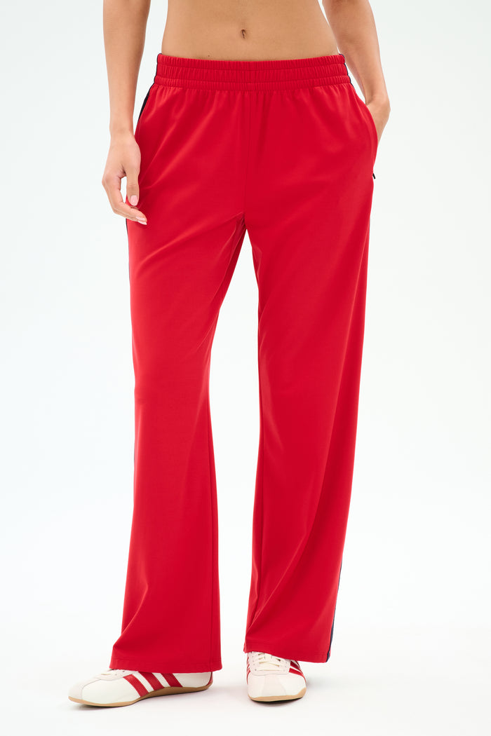 Model wears SPLITS59 Maxie Rigor Track Pant in Pirate Red/Indigo, wide leg style, paired with red-and-white sneakers, shown from waist to feet against a plain background.