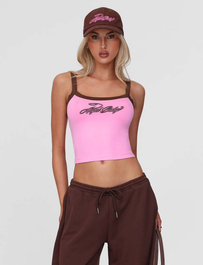 A woman poses against a gray background wearing a pink tank top with brown straps and “Baby Baby” text, brown sweatpants, and the TIGERMIST MERRYN CAP - CHOCOLATE.
